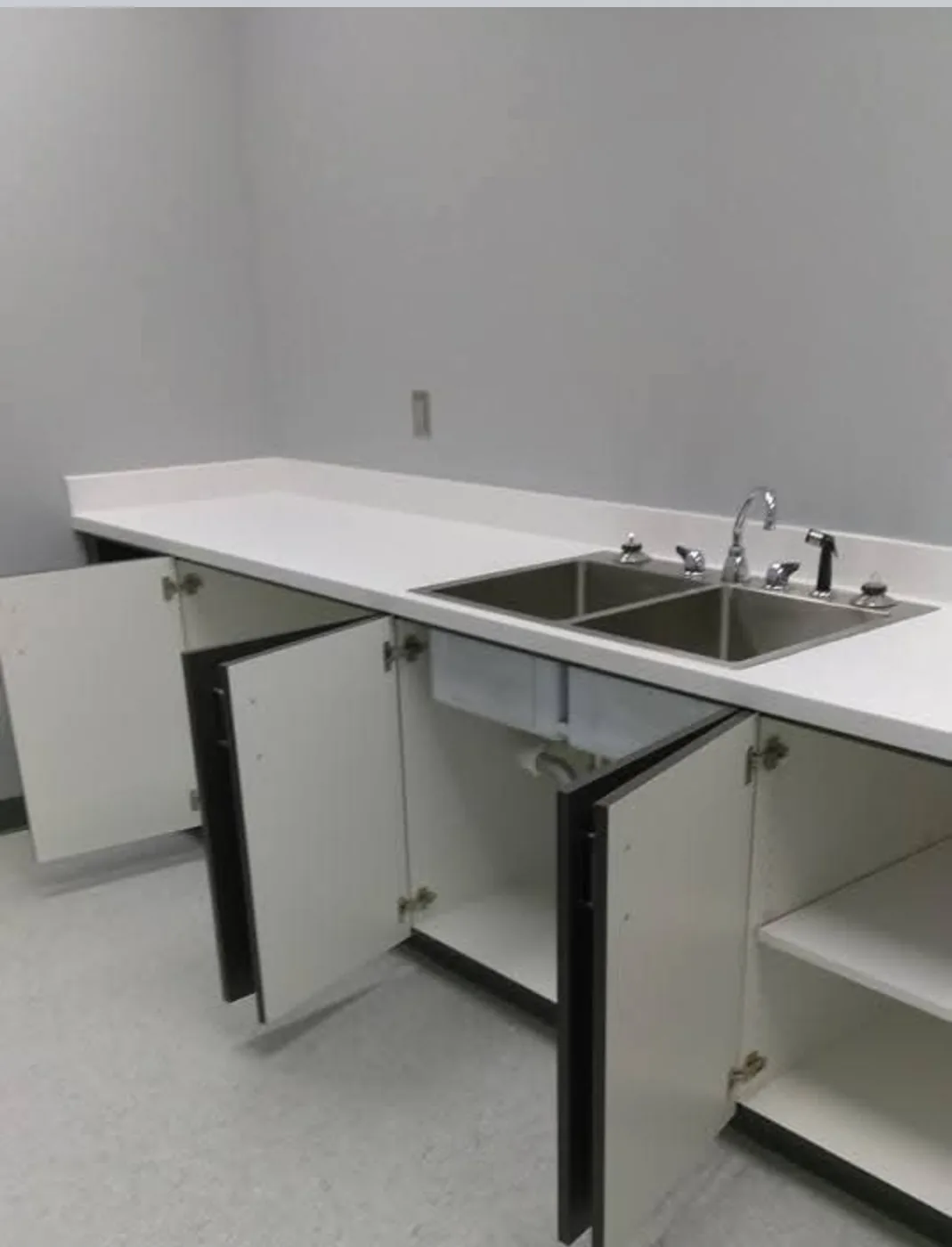A real Faithful Cleaning Service job - a facility break-room with a long white counter, a stainless double sink and clean white cabinets, freshly cleaned and detailed