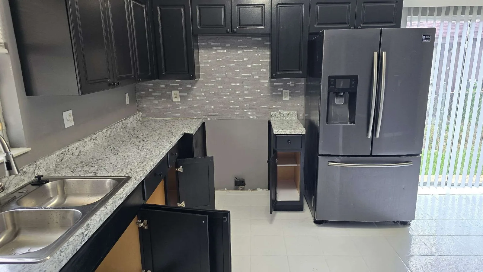 The finished kitchen wall run with repainted black cabinets, a new granite countertop and a tile backsplash